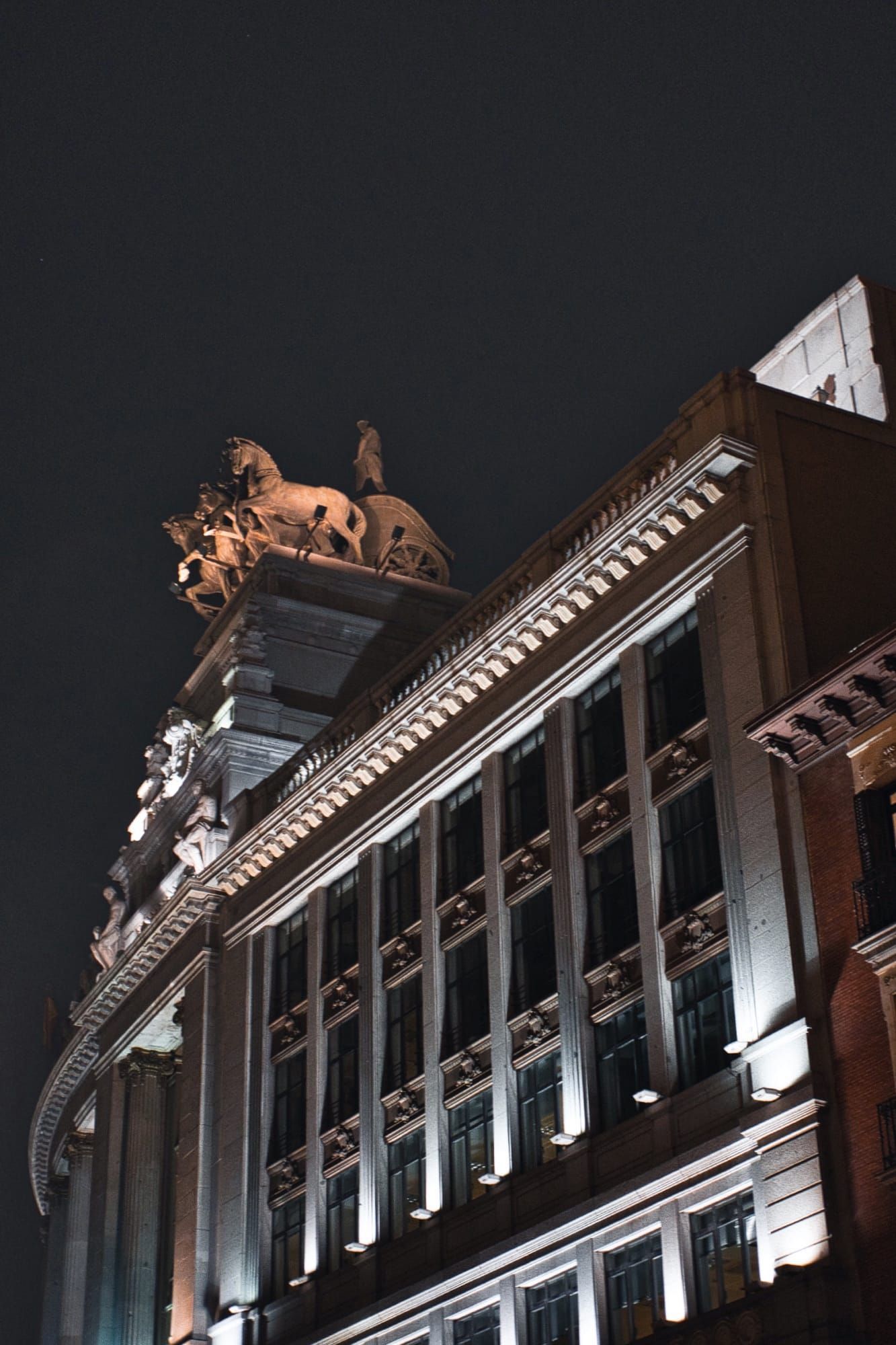 Ornate building at night with illuminated quadriga sculpture and chariot on top