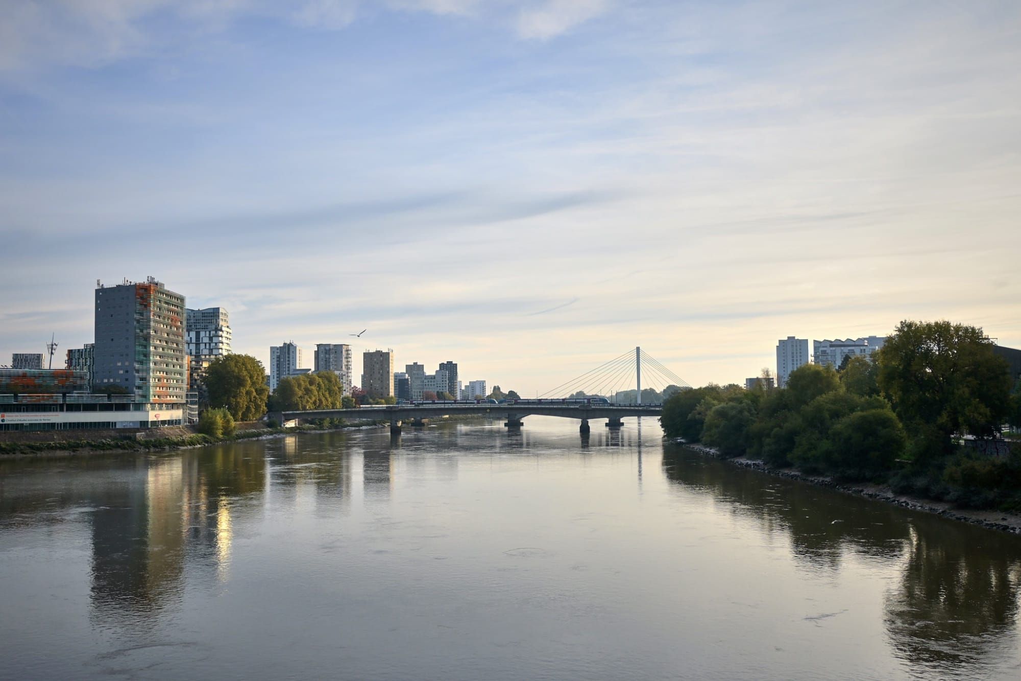 Panoramic city river with modern buildings, two bridges and green trees on right bank