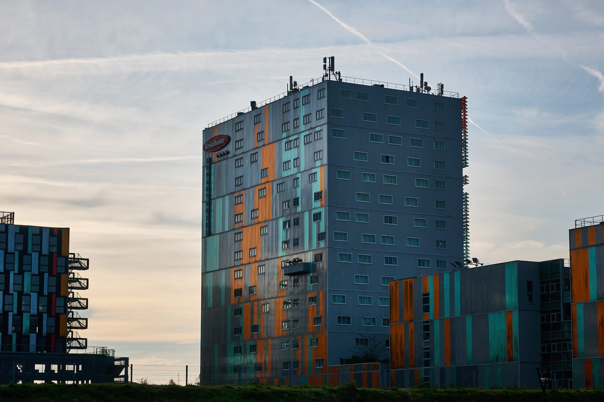 Modern high-rise with teal and orange paneling under partly cloudy sky