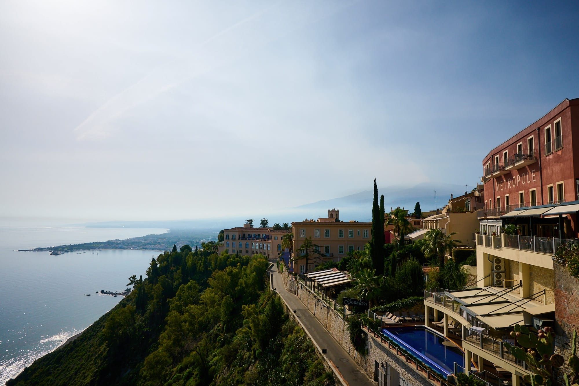 Mediterranean coastal town with terraced buildings, pool and blue sea from hillside