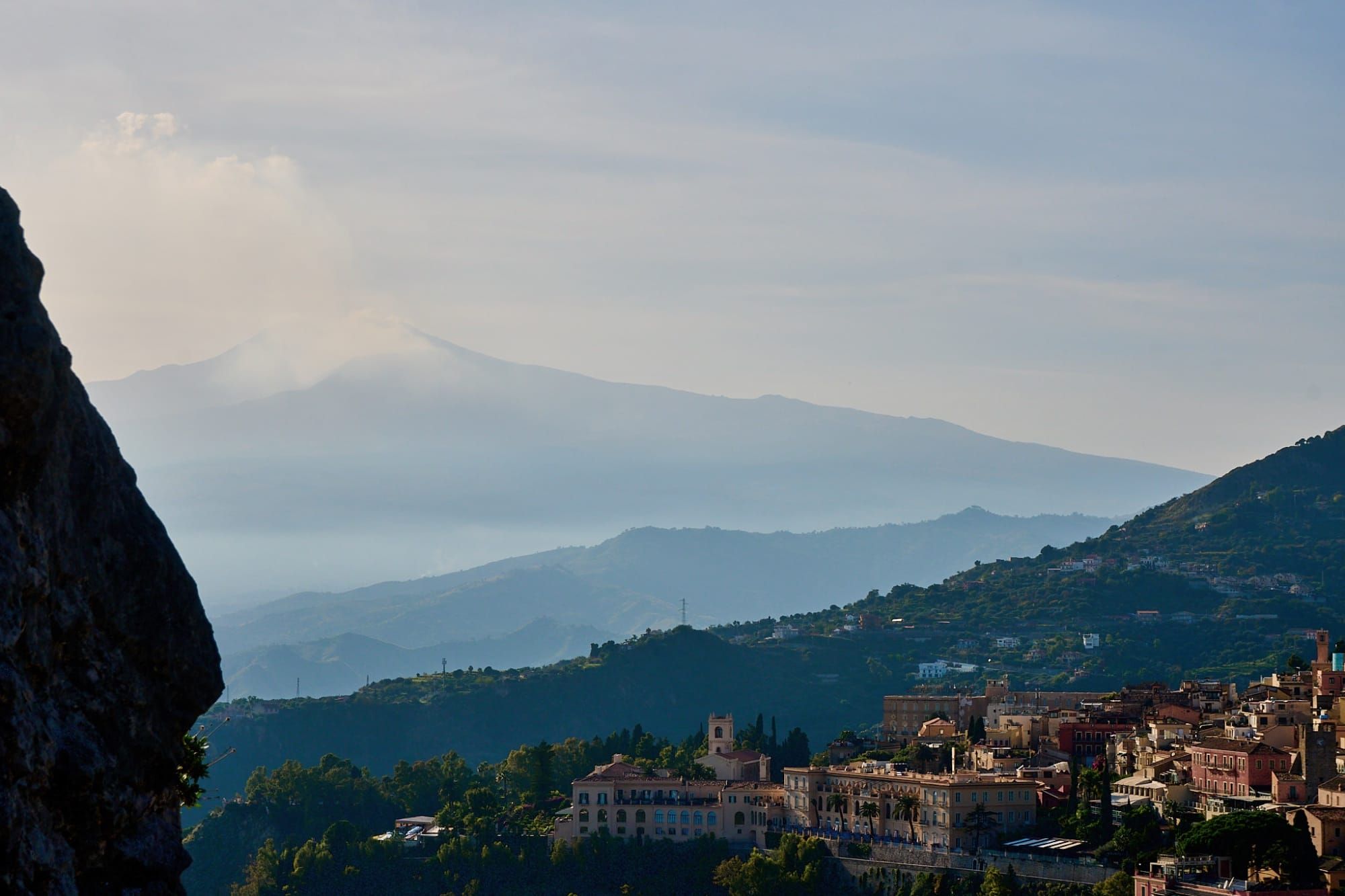 Hillside town with terracotta roofs and layered mountains under partly cloudy sky