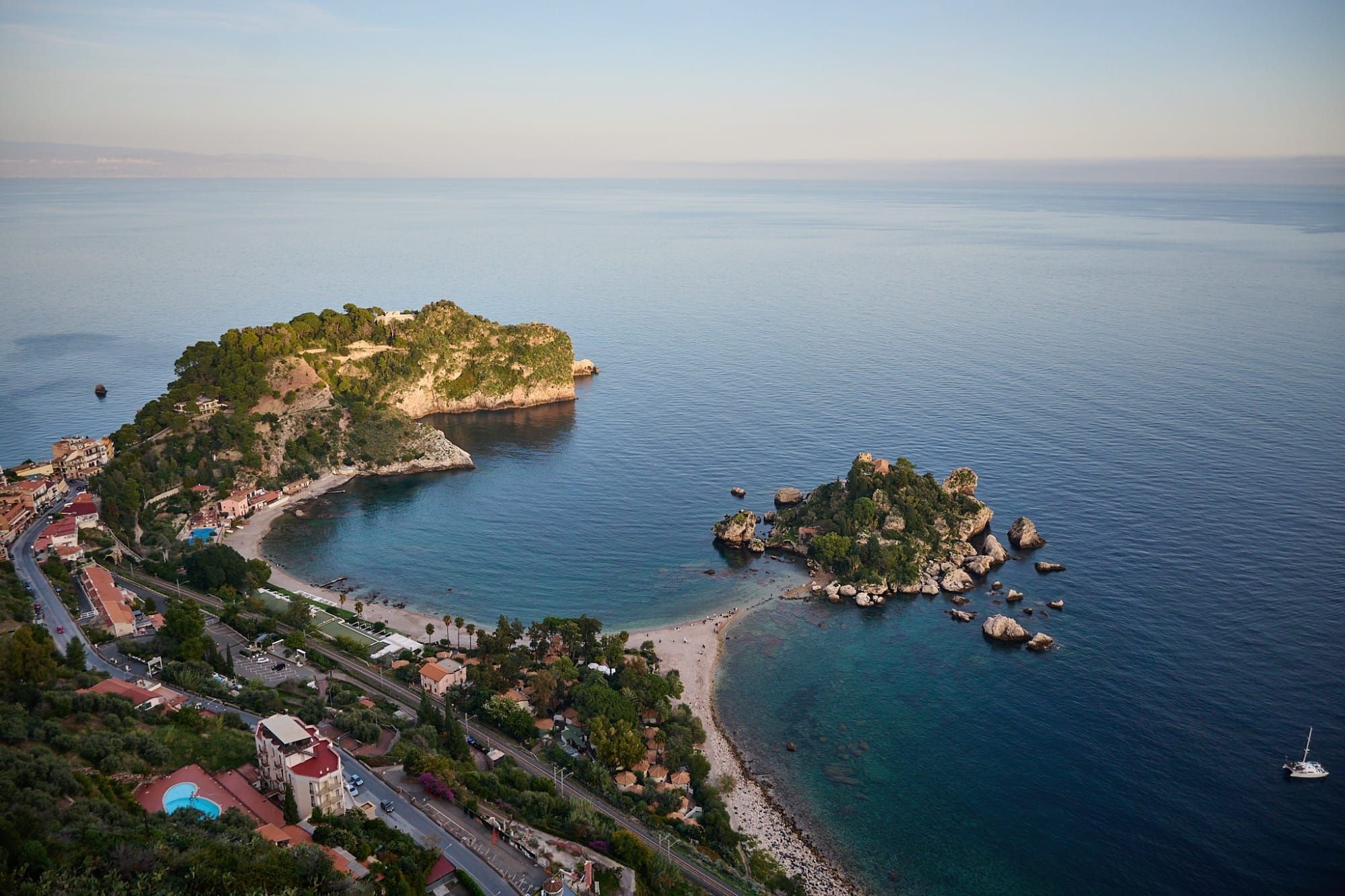 Aerial view of coastal bay with turquoise water, rocky islands and terracotta-roofed town