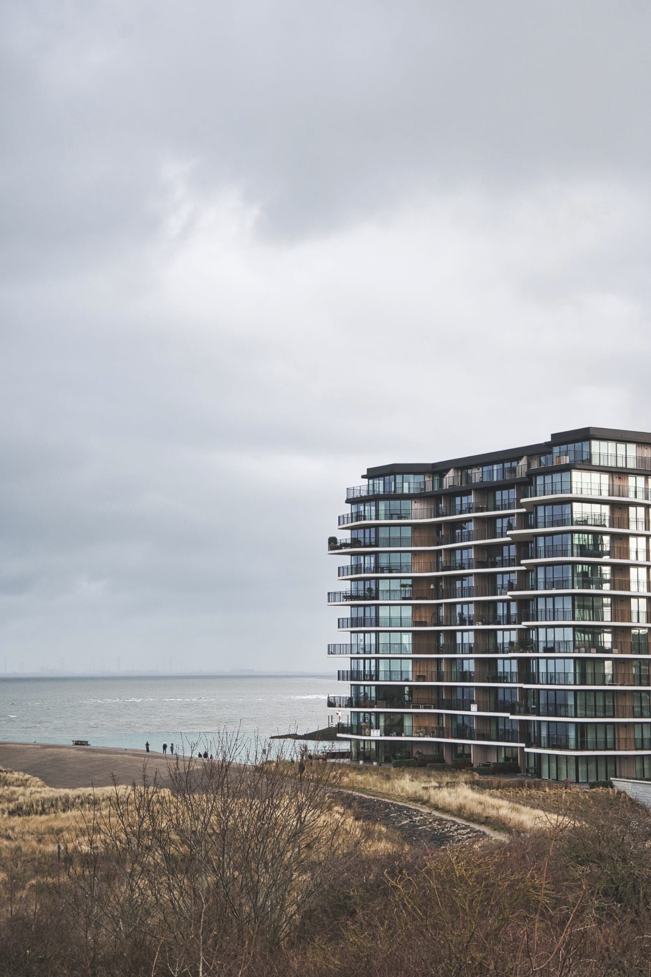 Modern glass apartment building overlooking grey sea and sandy beach on overcast day