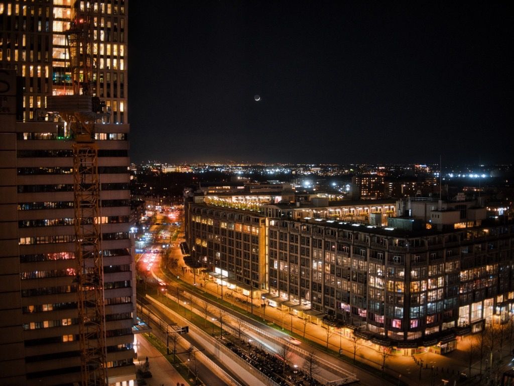 Night city view with lit buildings, street lights, and a thin crescent moon