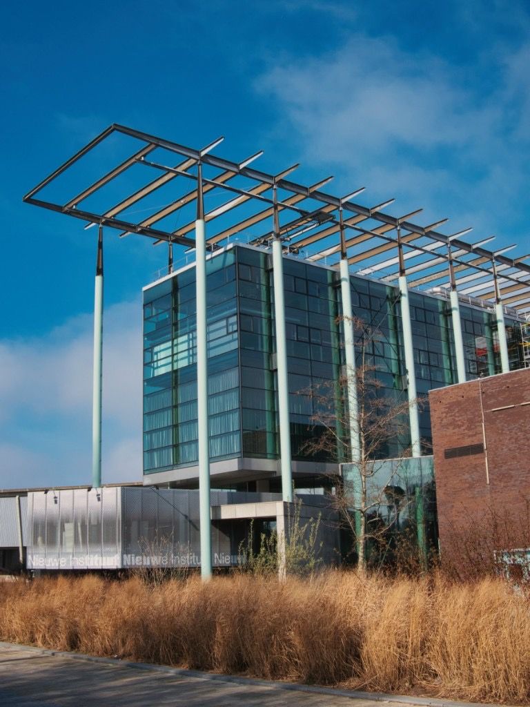 Modern glass building with tall pale green columns and dry grasses in front