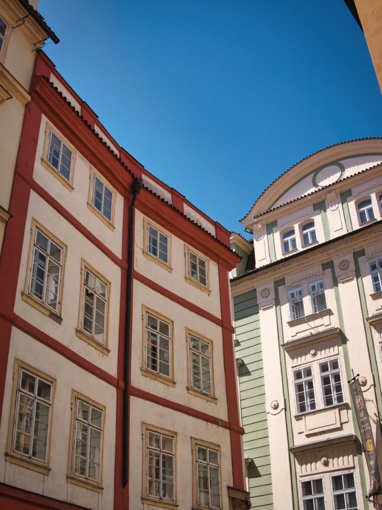Historic Prague buildings in warm tones framing a vivid blue sky from a low-angle street view
