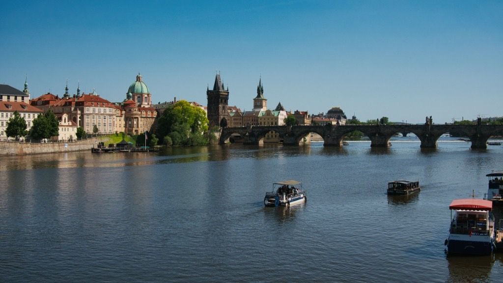 Panoramic view of the Vltava River in Prague with bridges, boats, and historic skyline under clear skies