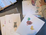 A bunch of drawings, includes a duck and mouse in a cute manner, next to it you see a child's arms drawing/colouring some cute animals