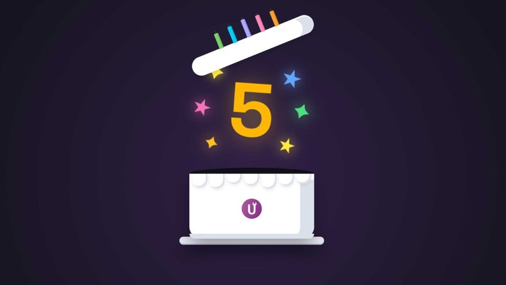 A white cake with a purple U logo beneath a popping lid, a yellow number five, and colourful stars.